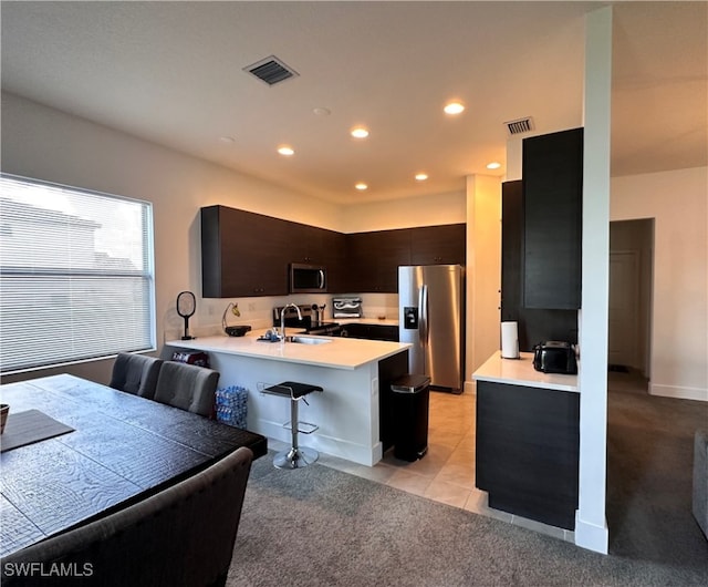 kitchen with light carpet, appliances with stainless steel finishes, kitchen peninsula, and a breakfast bar area