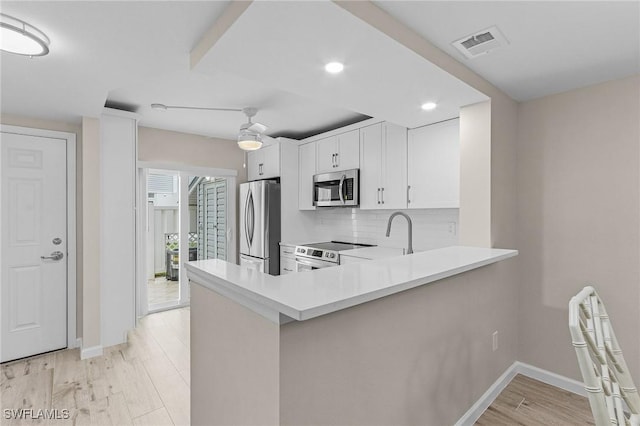 kitchen featuring light wood-style flooring, stainless steel appliances, visible vents, light countertops, and backsplash