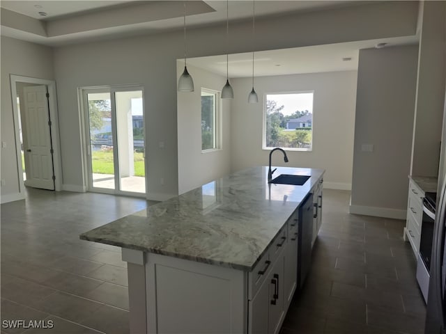 kitchen featuring sink, white cabinets, hanging light fixtures, a center island with sink, and light stone countertops