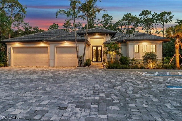 prairie-style house featuring french doors, decorative driveway, an attached garage, and stucco siding