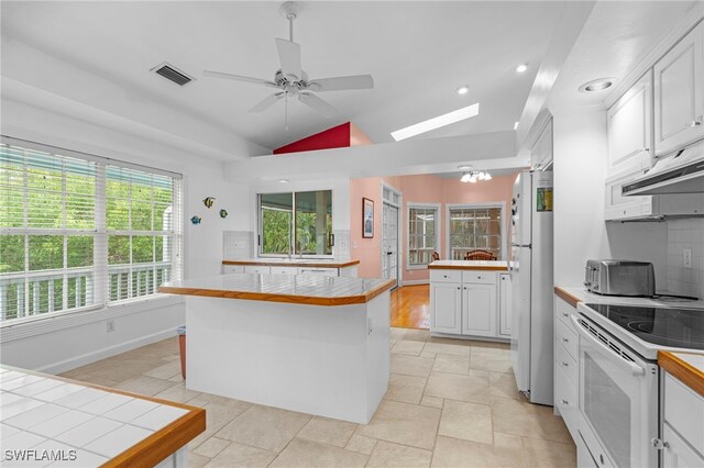 kitchen featuring a center island, white appliances, vaulted ceiling, tile counters, and white cabinetry