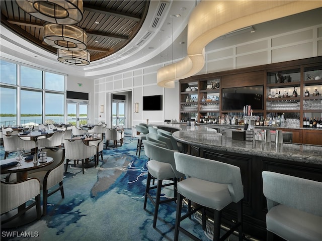 bar featuring carpet, dark stone countertops, and a high ceiling