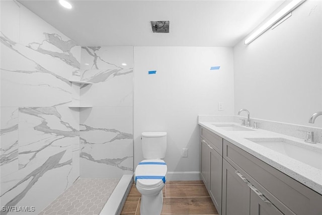 bathroom with a tile shower, hardwood / wood-style floors, vanity, and toilet