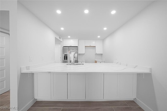 kitchen with kitchen peninsula, stainless steel refrigerator with ice dispenser, light stone countertops, sink, and white cabinetry