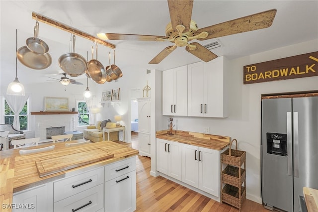 kitchen featuring a fireplace, white cabinetry, butcher block countertops, stainless steel fridge, and ceiling fan