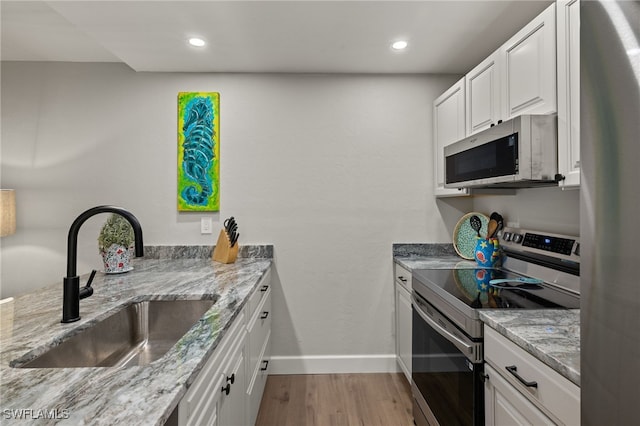 kitchen with light stone countertops, stainless steel appliances, light hardwood / wood-style floors, white cabinetry, and sink