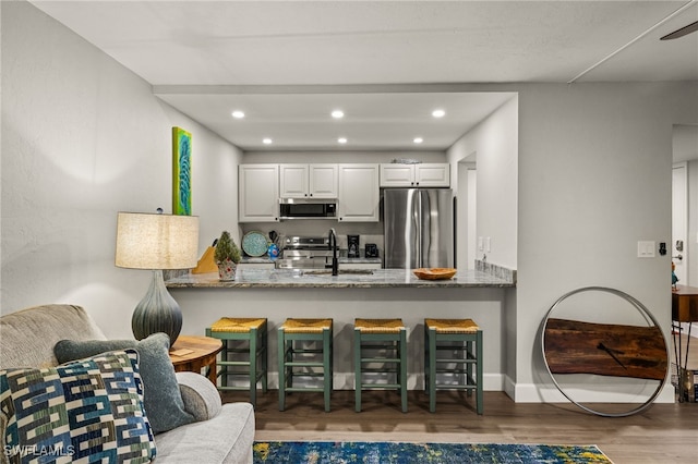 kitchen featuring white cabinetry, stone counters, kitchen peninsula, wood-type flooring, and appliances with stainless steel finishes