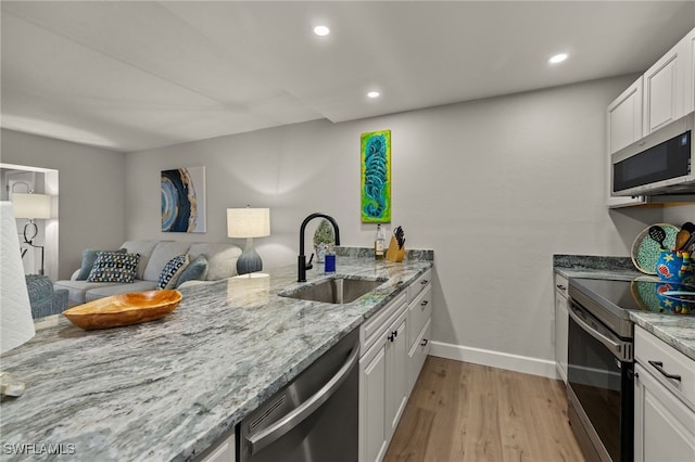 kitchen with appliances with stainless steel finishes, light wood-type flooring, kitchen peninsula, sink, and white cabinetry