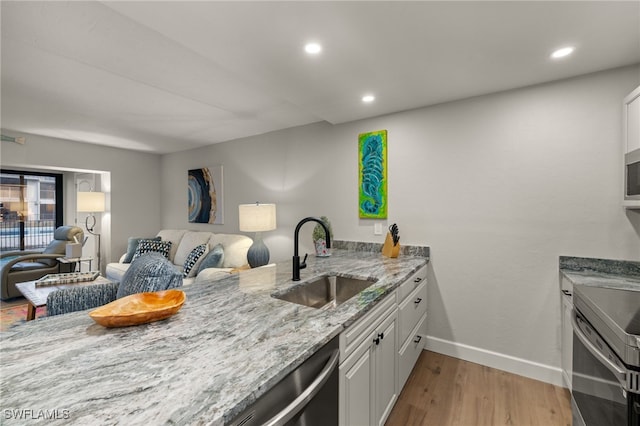 kitchen featuring sink, white cabinets, light stone counters, light wood-type flooring, and appliances with stainless steel finishes