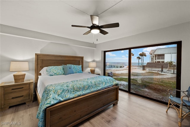 bedroom featuring access to outside, ceiling fan, light hardwood / wood-style flooring, and a water view