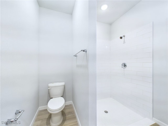 bathroom with hardwood / wood-style floors, toilet, and a tile shower