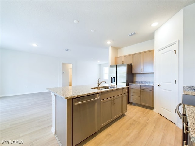 kitchen with stainless steel appliances, sink, light stone counters, a center island with sink, and light wood-type flooring