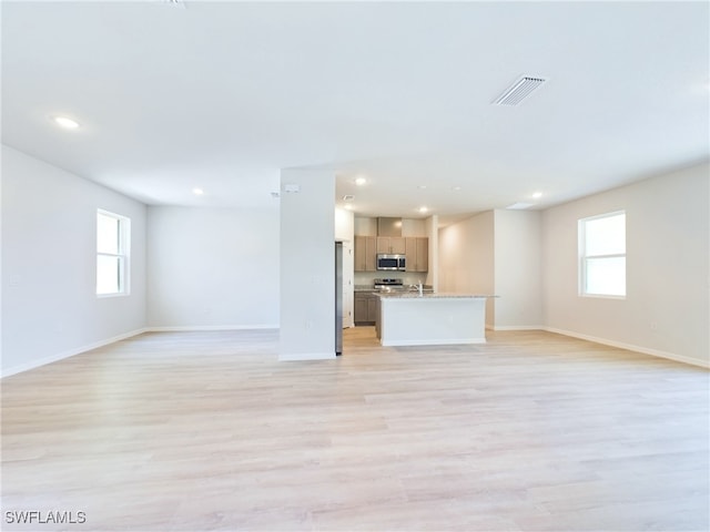 unfurnished living room featuring sink, plenty of natural light, and light hardwood / wood-style floors