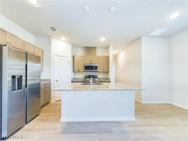 kitchen featuring light wood-type flooring, appliances with stainless steel finishes, an island with sink, and light stone countertops