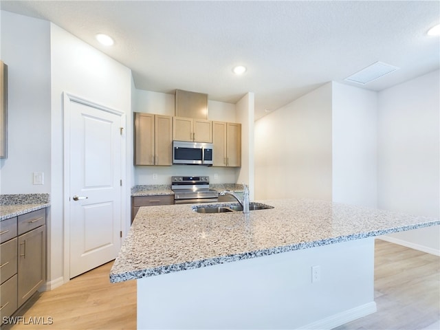 kitchen featuring stainless steel appliances, light hardwood / wood-style flooring, a center island with sink, and light stone countertops