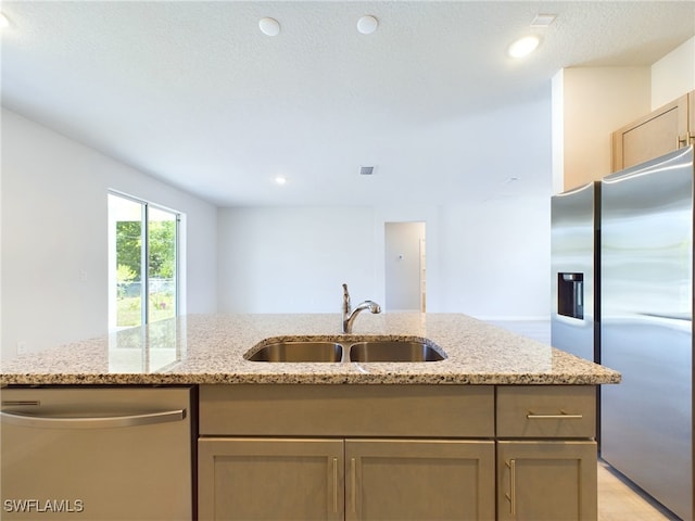 kitchen with appliances with stainless steel finishes, sink, light stone counters, and a center island with sink