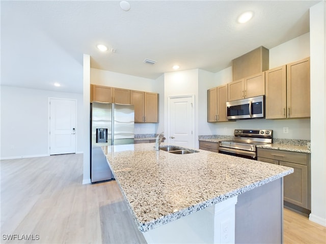 kitchen featuring stainless steel appliances, light hardwood / wood-style floors, sink, an island with sink, and light stone countertops