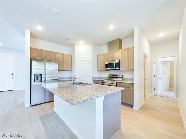 kitchen featuring light hardwood / wood-style flooring, a kitchen island with sink, appliances with stainless steel finishes, light stone counters, and sink