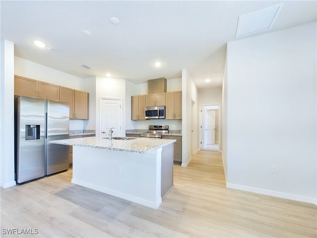 kitchen with sink, appliances with stainless steel finishes, light stone countertops, an island with sink, and light hardwood / wood-style floors