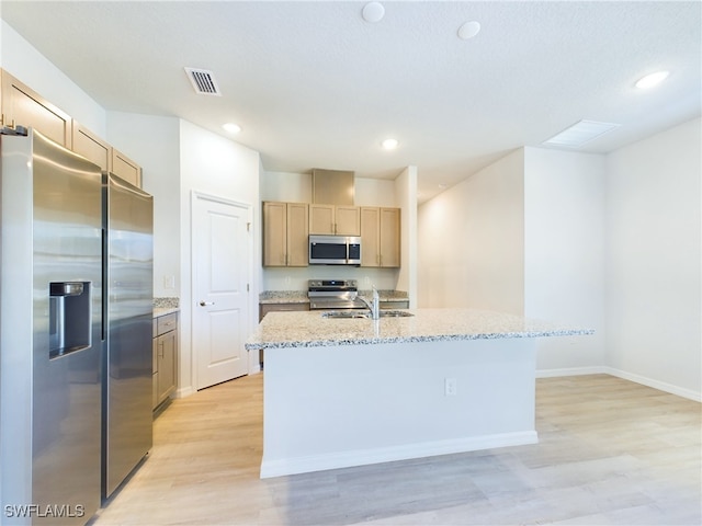 kitchen featuring light hardwood / wood-style flooring, an island with sink, light stone countertops, and stainless steel appliances