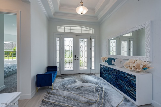 foyer with french doors, a raised ceiling, ornamental molding, and light hardwood / wood-style flooring