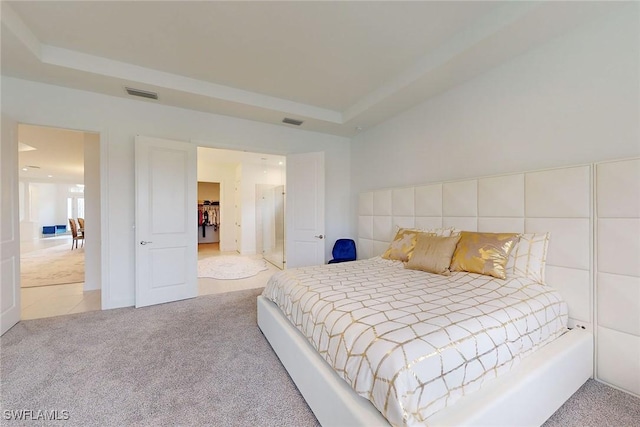 bedroom with carpet, visible vents, and a tray ceiling