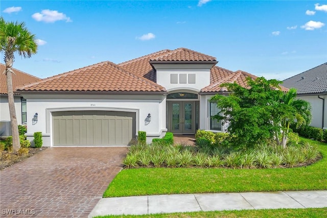 mediterranean / spanish house with a garage, a tile roof, decorative driveway, french doors, and stucco siding