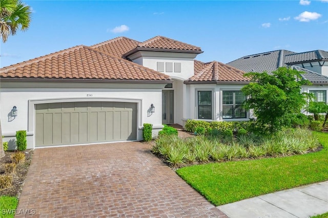 mediterranean / spanish home with a tiled roof, decorative driveway, an attached garage, and stucco siding