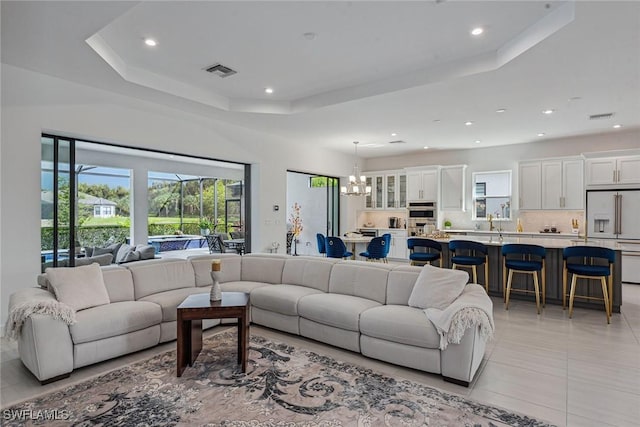 living area featuring an inviting chandelier, light tile patterned floors, visible vents, and a raised ceiling