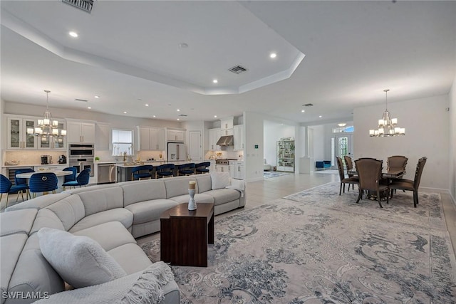 living room with a tray ceiling, visible vents, and a notable chandelier