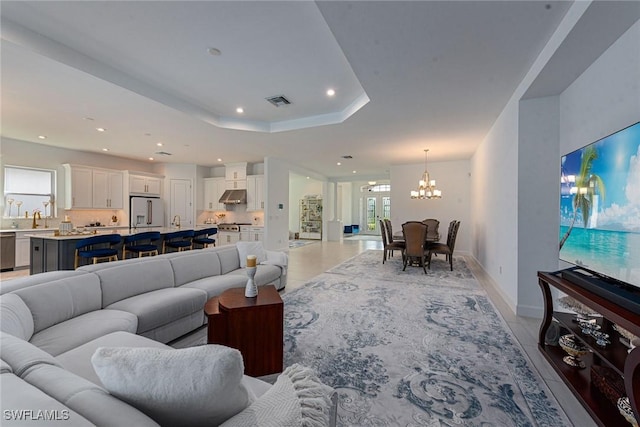 living room featuring a tray ceiling, recessed lighting, visible vents, an inviting chandelier, and baseboards