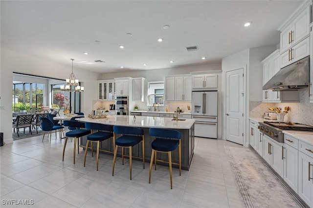 kitchen featuring visible vents, appliances with stainless steel finishes, under cabinet range hood, a kitchen bar, and a sink