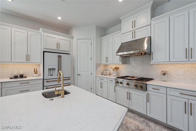 kitchen with high end white refrigerator, stainless steel gas stovetop, backsplash, a sink, and under cabinet range hood