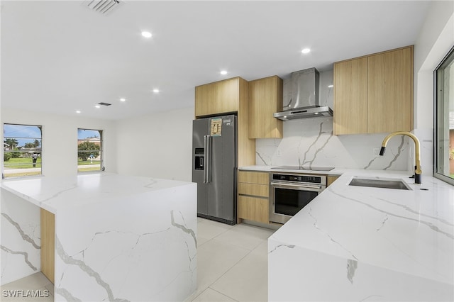 kitchen with sink, appliances with stainless steel finishes, decorative backsplash, light stone countertops, and wall chimney range hood