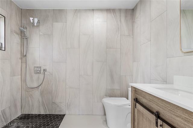 bathroom featuring tile walls, toilet, a tile shower, and vanity