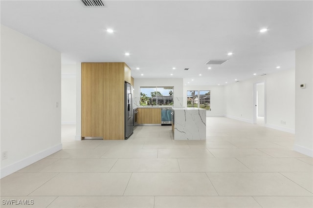 kitchen with kitchen peninsula, stainless steel appliances, light tile patterned floors, and light stone counters