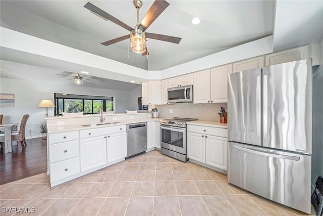 kitchen with appliances with stainless steel finishes, white cabinets, kitchen peninsula, ceiling fan, and sink