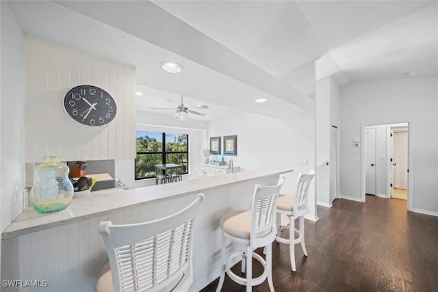 kitchen with ceiling fan, vaulted ceiling, kitchen peninsula, and dark hardwood / wood-style flooring