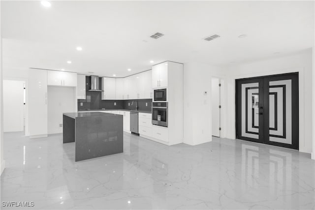 kitchen featuring wall chimney range hood, white cabinetry, stainless steel appliances, a center island, and decorative backsplash