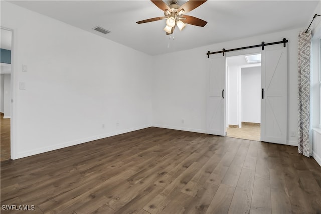 spare room with dark hardwood / wood-style flooring, ceiling fan, and a barn door