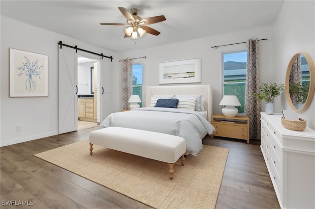 bedroom featuring ceiling fan, a barn door, dark hardwood / wood-style floors, and ensuite bath