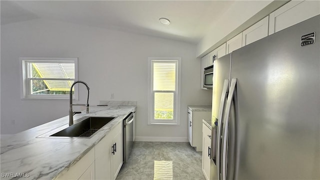 kitchen featuring appliances with stainless steel finishes, light stone counters, sink, white cabinets, and lofted ceiling