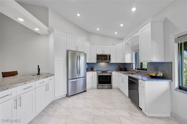 kitchen featuring light stone countertops, stainless steel appliances, vaulted ceiling, sink, and white cabinets