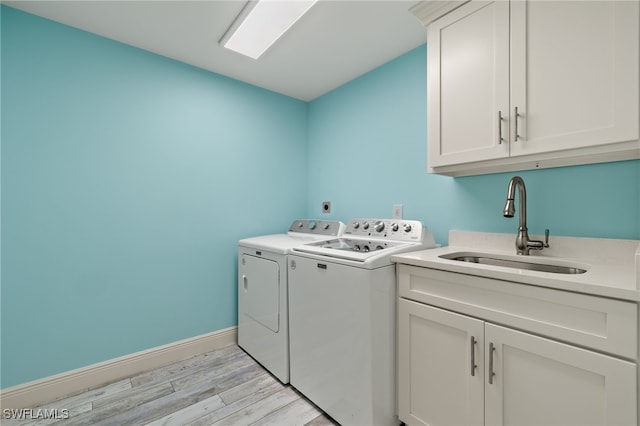 laundry room featuring washing machine and clothes dryer, cabinets, sink, and light hardwood / wood-style floors