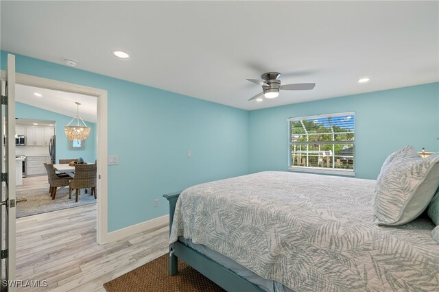 bedroom featuring lofted ceiling, ceiling fan with notable chandelier, stainless steel refrigerator, and light hardwood / wood-style flooring