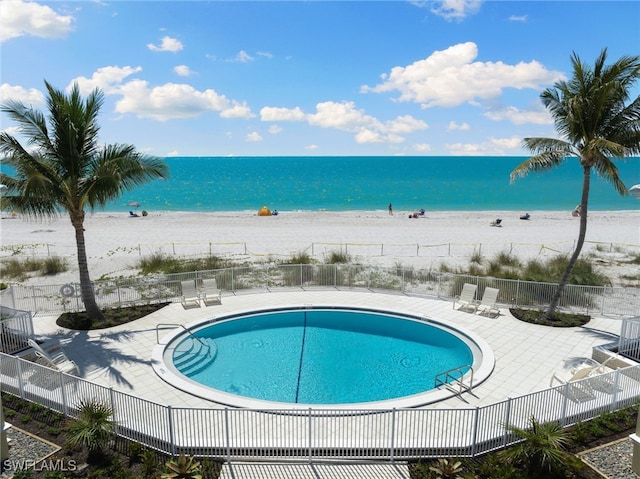 view of pool featuring a patio area, a water view, and a beach view