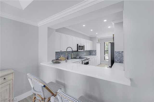 kitchen featuring kitchen peninsula, ornamental molding, tasteful backsplash, white cabinetry, and stainless steel appliances