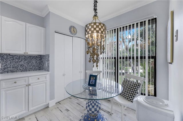 interior space featuring hanging light fixtures, white cabinetry, crown molding, light hardwood / wood-style floors, and decorative backsplash