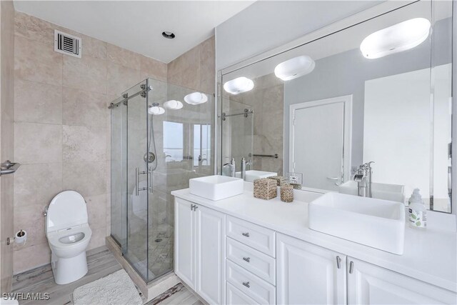 bathroom with vanity, toilet, a shower with shower door, tile walls, and hardwood / wood-style floors