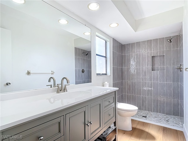 bathroom featuring wood-type flooring, a tile shower, vanity, and toilet